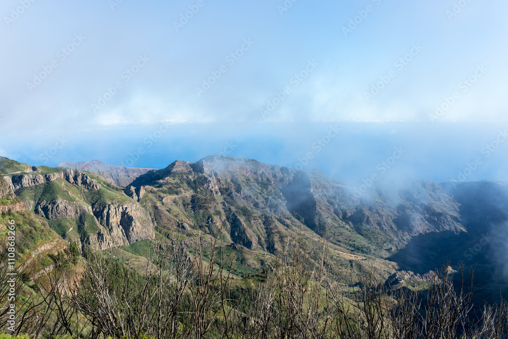 Obraz premium Barranco de Benchijigua on the Canary island La Gomera in clouds, which were formed above regions within trade wind. The clouds comes from the Azores and reaches the Islands in approx. 800m altitude