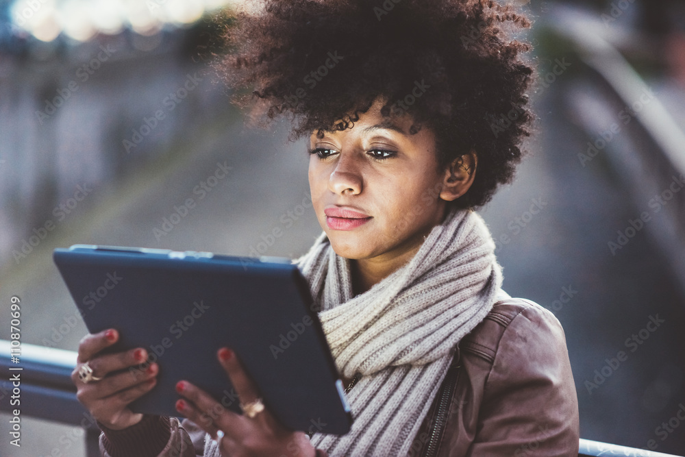 Half length of beautiful black curly hair african woman using tablet in town by night, face illuminated by screen light - technology, communication, social network concept