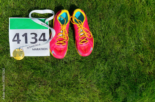 Running shoes, marathon race bib (number) and finisher medal on grass background, sport, fitness and healthy lifestyle concept 