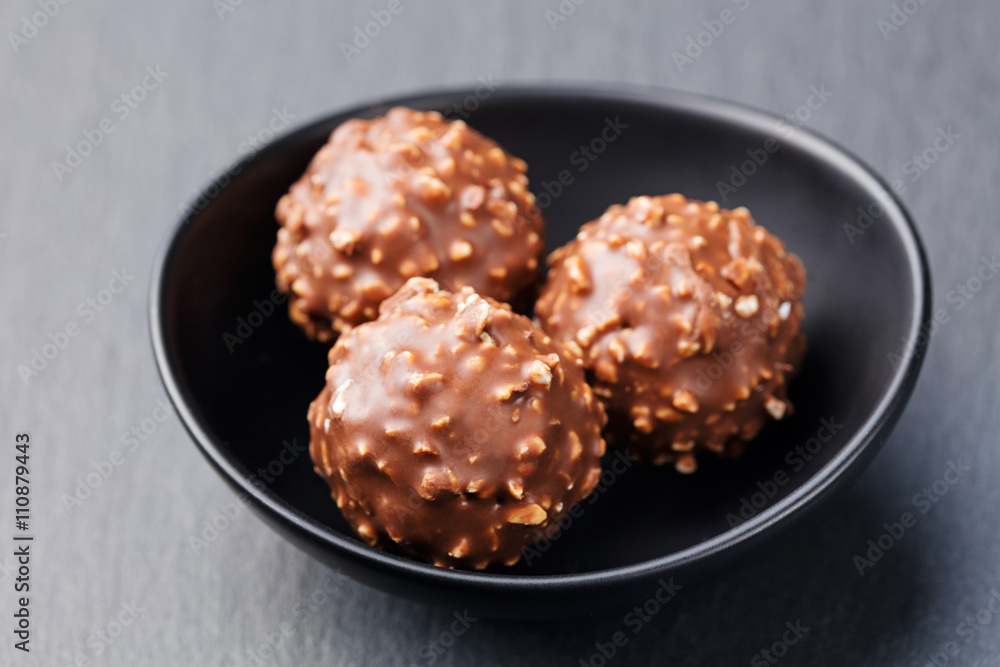 Chocolate candies, truffle in ceramic black bowl on grey slate background Copy space.