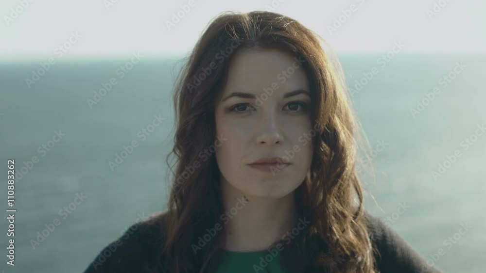 Beautiful woman looking at the camera standing on a background of sea and mountains Beautiful woman looking at the camera standing on a background of sea and mountains