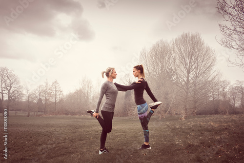 Full length side view of women face to face on one leg, hands on each others shoulders photo