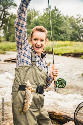 Woman by river  arm raised holding freshly caught fish, looking at camera smiling photo
