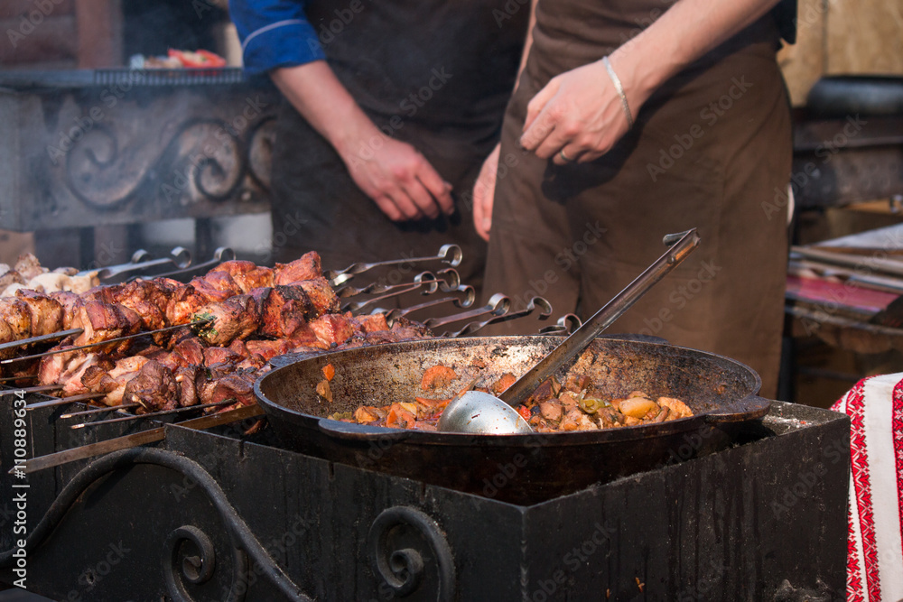 street food - ratatouille in a old cauldron and ladle, barbecue grill on skewers on brazier, chefs on background street food - ratatouille in a old cauldron and ladle, barbecue grill on skewers on brazier, chefs on background
