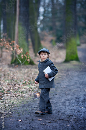 Cute little child, holding lantern and book in forest