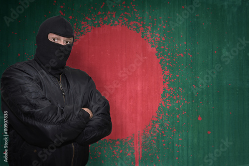 dangerous man in a mask standing near a wall with painted national flag of bangladesh