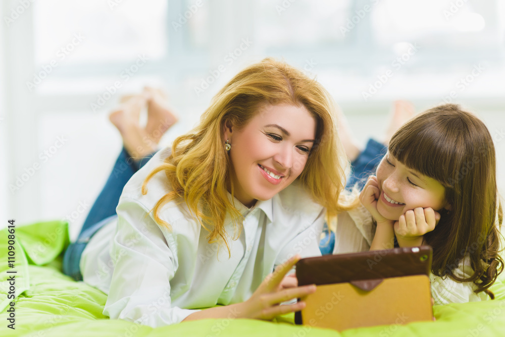 happy family. Mother and daughter sitting on the bed with a tablet happy family. Mother and daughter sitting on the bed with a tablet