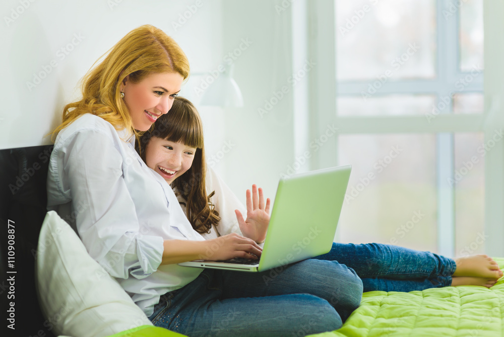 happy family. Mother and daughter sitting on the bed with a laptop happy family. Mother and daughter sitting on the bed with a laptop