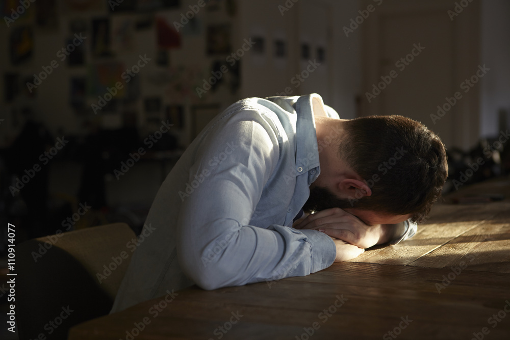 © Connect Images - Young man sitting at kitchen table with his head down © Connect Images - Young man sitting at kitchen table with his head down
