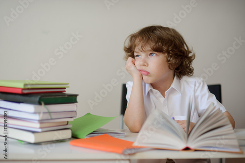 Daydreaming schoolboy sits at a school desk