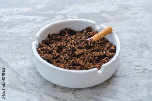 Cigarette and coffee ground on the ceramic ashtray.