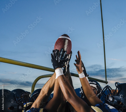 Victorious teenage and young male american football team holding up ball photo
