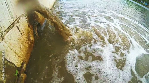 Dirty  water flows from a pipe into the river. The drain carries sewage