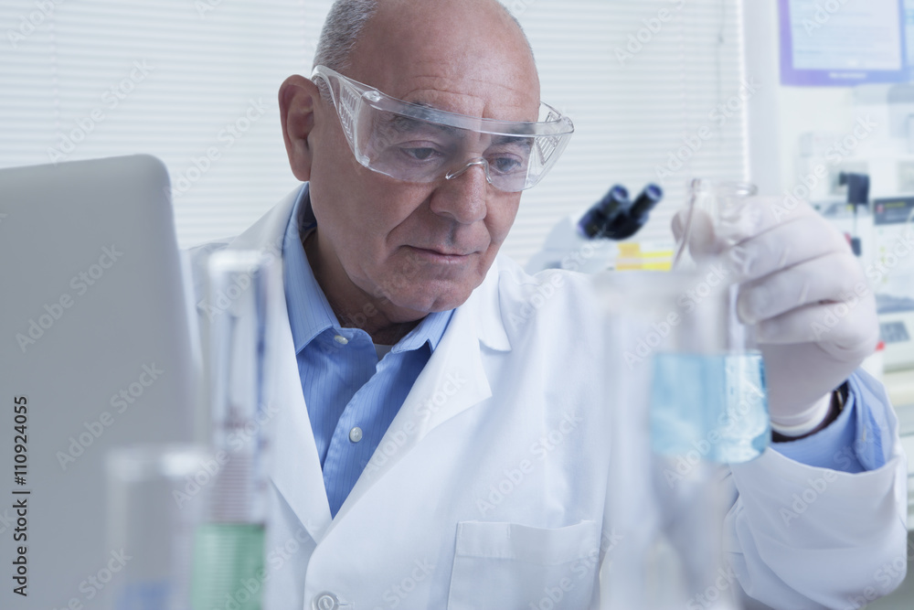 Senior male scientist looking at flask, containing blue liquid Senior male scientist looking at flask, containing blue liquid