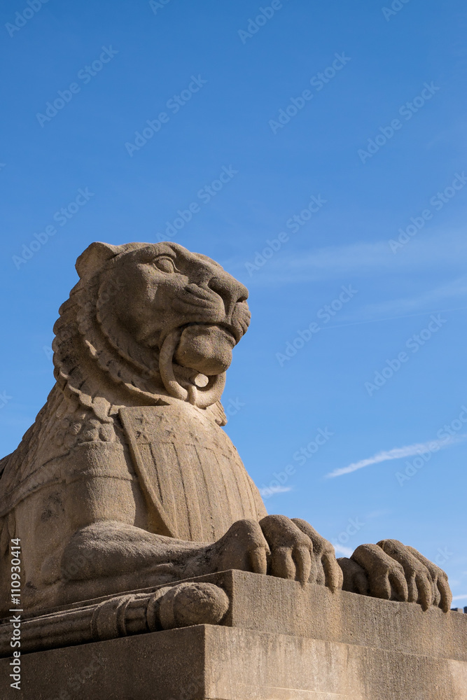 Laying lion statue on a pedestal against a blue sky
