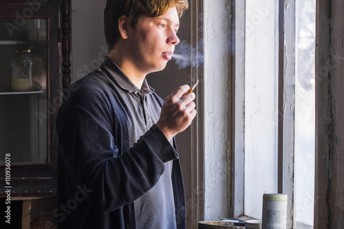 Male artist smoking cigarette whist staring out of studio window