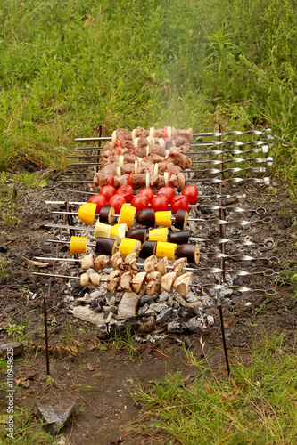 Cooking kebabs and tomatoes on skewers outdoors.
