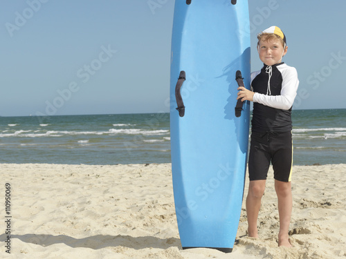 Portrait of boy nipper (child surf life savers) next to surfboard, Altona, Melbourne, Australia