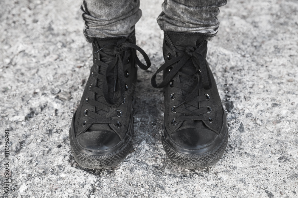 Feet in black gumshoes stand on gray ground