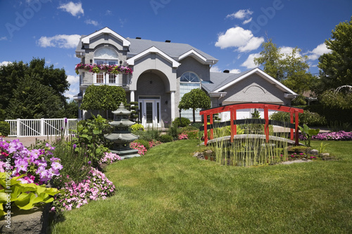 Grey brick cottage style residential home and landscaped  manicured garden with red footbridge, Quebec, Canada photo