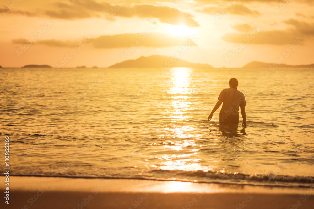 Woman walking in the sea in sunset