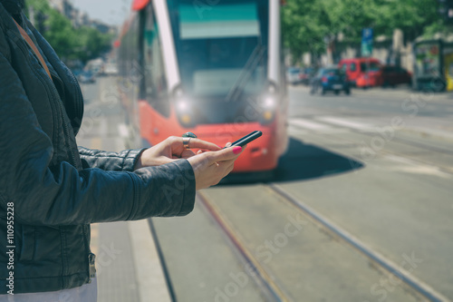 Girl using smartphone on a station with defocused tramway. photo