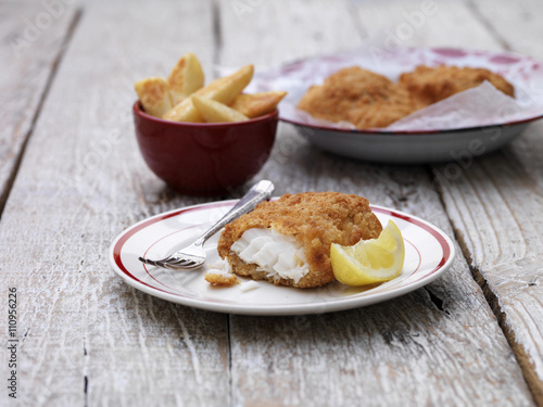 Breaded chunky cod with bowl of french fries on wooden table