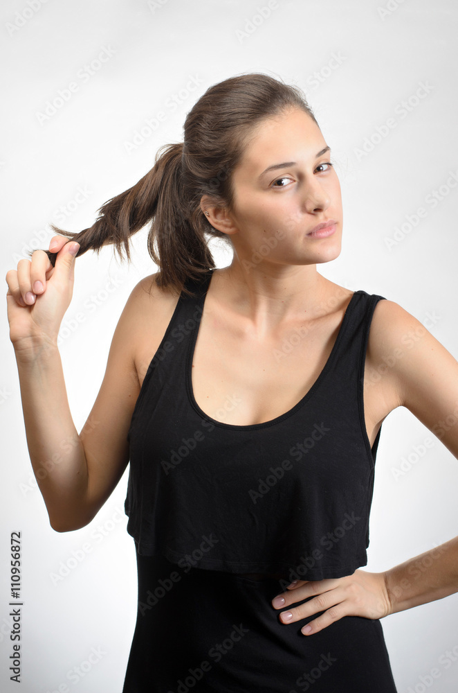 Portrait of a beautiful young woman touching her hair standing against grey background Portrait of a beautiful young woman touching her hair standing against grey background