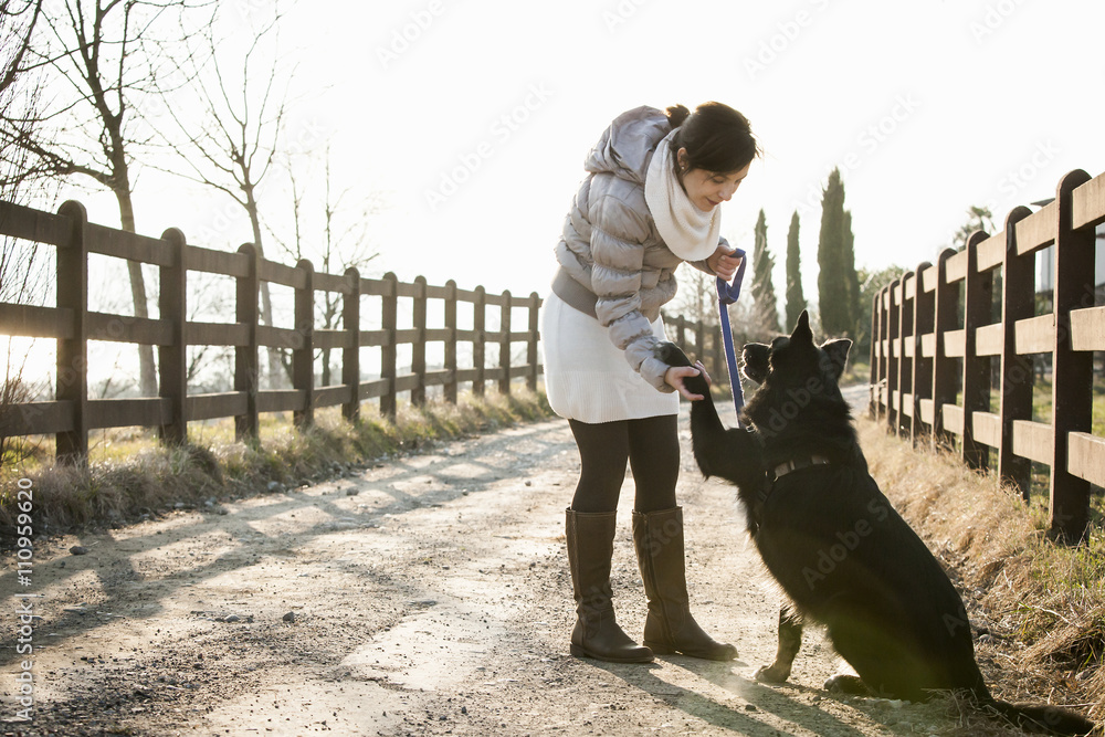 © Connect Images - Mid adult woman training her dog to hold up paw on rural road