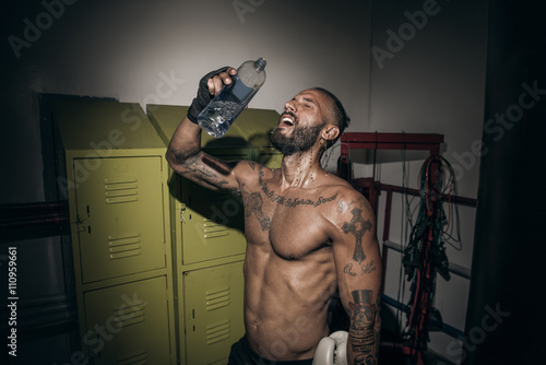 Tattooed male boxer pouring water on face in gym photo