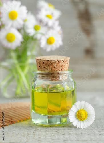 Small bottle of cosmetic chamomile oil and wooden hair comb