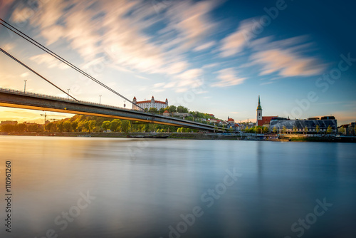 Bratislava cityscape view on old town with castle, bridge and St. Martin's cathedral from the opposite side of Danube river at the sunset. Long exposure technique with smooth water