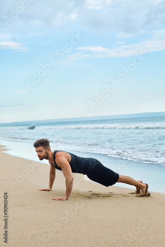 Sports. Sporty Handsome Male Doing Push Ups Exercise During Outdoor Workout At Beach. Fit Athletic Man With Muscular Body Exercising On Sand, Training Near Ocean. Fitness, Healthy Lifestyle Concept © puhhha