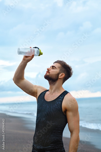Tired Man Pouring Refreshing Water Over Face, Resting After Running Workout At Beach. Portrait Of Healthy Athletic Male After Exercising Outdoor On Hot Summer Day. Sports, Fitness Concept
