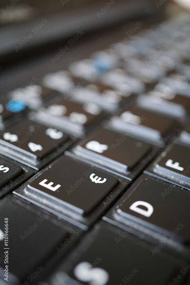 Detail of a black dusty laptop keyboard with a focus on a sign of Euro currency Detail of a black dusty laptop keyboard with a focus on a sign of Euro currency