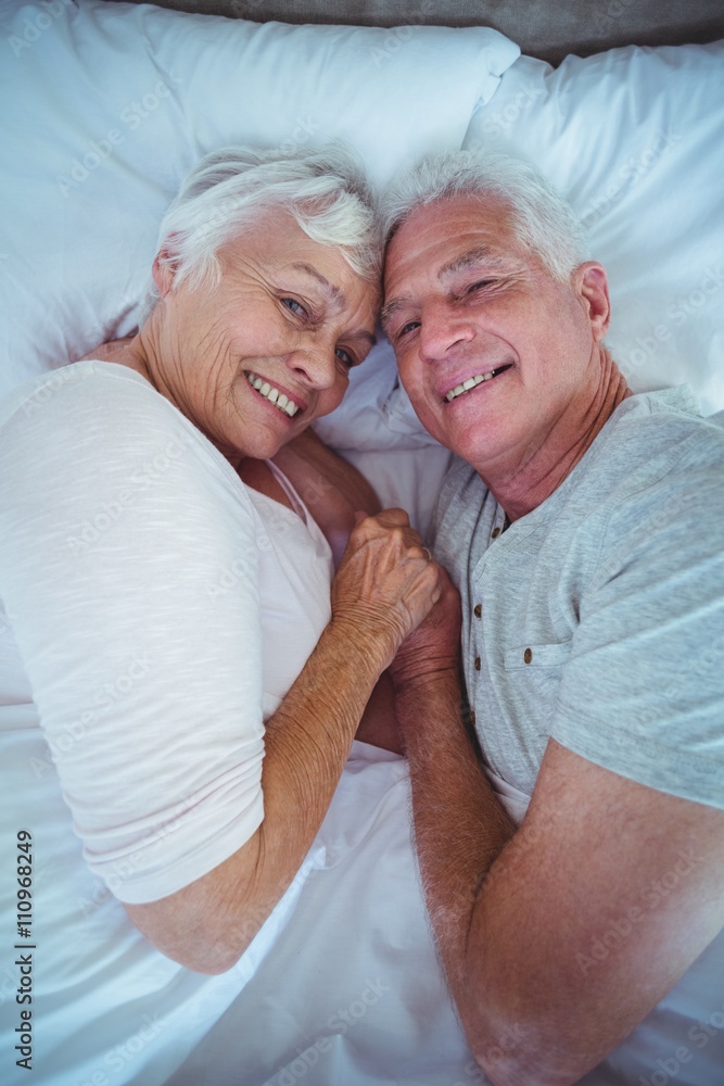 Portrait of senior couple holding hands while lying on bed Portrait of senior couple holding hands while lying on bed