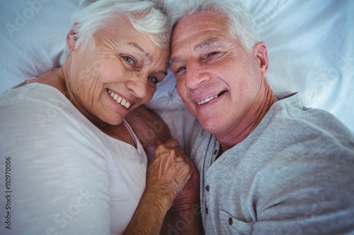 Senior couple holding hands while lying on bed