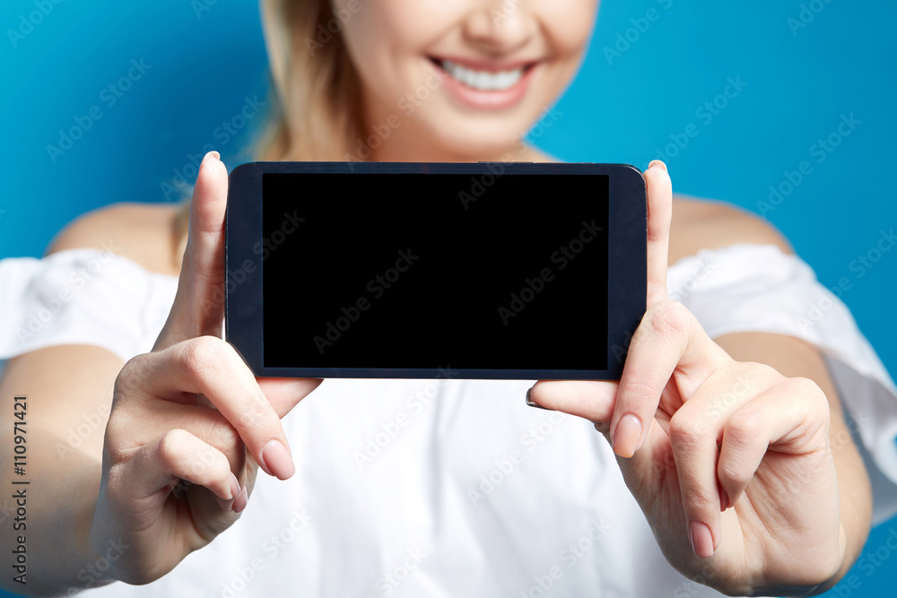 Young smiling woman showing screen of phone on blue background. Close up