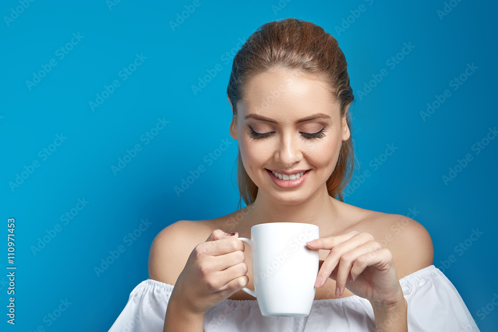Beautiful young woman holding a white cup of drink and smiling on blue background Beautiful young woman holding a white cup of drink and smiling on blue background