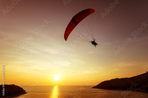 Silhouette of sky diver flies on background of sunset sky and sea. Phuket island, Thailand