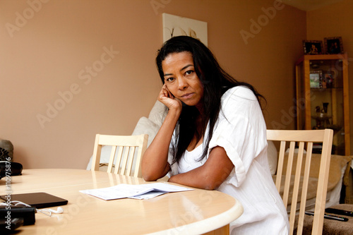 Portrait of fed up mature woman sitting at dining table reading bill photo