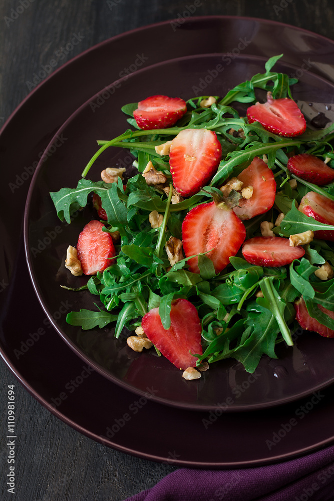 Fresh salad with strawberry, arugula and walnuts on purple plate. Low key Fresh salad with strawberry, arugula and walnuts on purple plate. Low key
