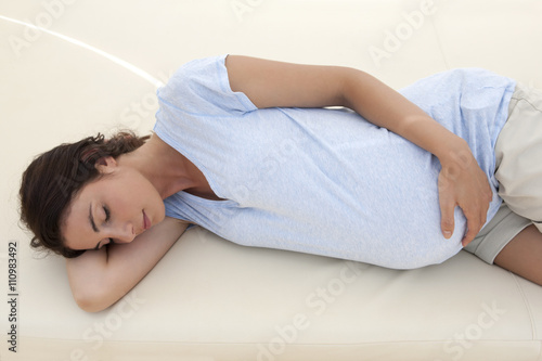 Pregnant mid adult woman sleeping on daybed with hand on stomach