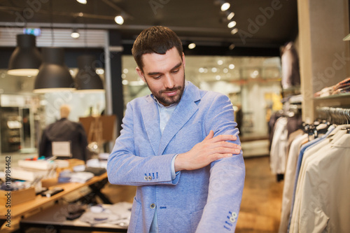 happy young man trying jacket on in clothing store