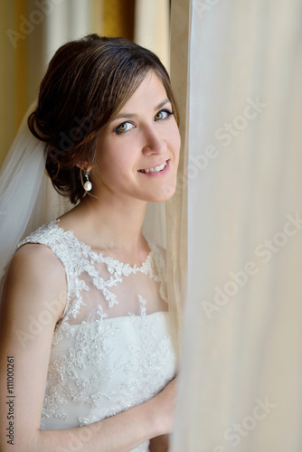 Beauty bride in bridal gown with lace veil indoors. Beautiful model girl in a white wedding dress. Female portrait of cute lady. Woman with hairstyle