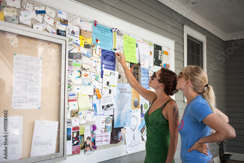 Two mid adult women looking up at community notice board