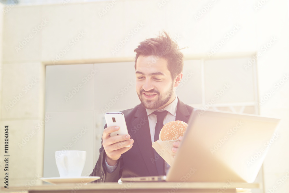 Closeup toned image of happy businessman looking at his mobile or smart phone while sitting in restaurant or cafe in front of laptop computer. Closeup toned image of happy businessman looking at his mobile or smart phone while sitting in restaurant or cafe in front of laptop computer.