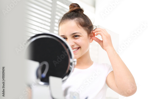 Niewidoczny aparat słuchowy. Wesoła dziewczynka zakłada aparat słuchowy przeglądając się w lusterku