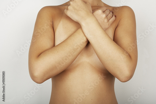 Neck down studio portrait of naked mid adult woman with arms across her chest photo