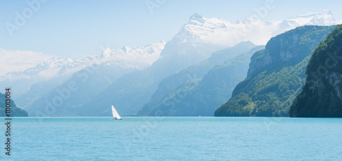 Grandiose mountain landscape. Mountain tops in the snow. White sail on a romantic lake.